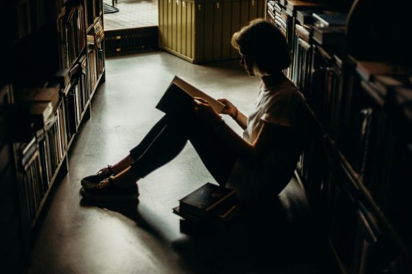 A young woman engrossed in a book, sitting on the floor of a quiet library, creating a cozy reading atmosphere.
