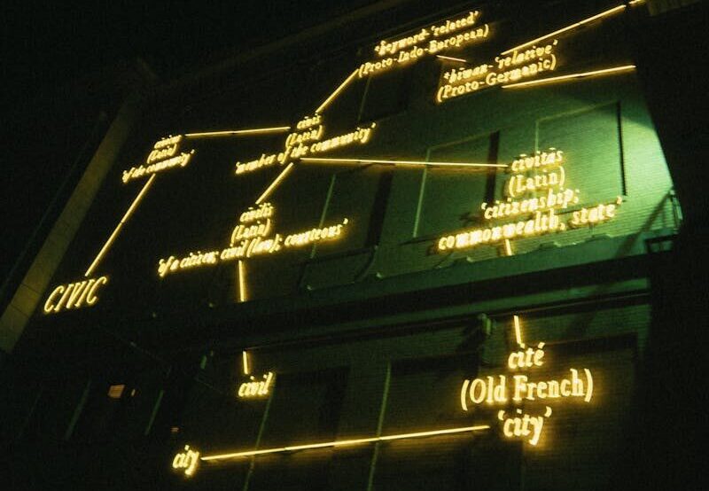 Neon-lit structure at night displaying historical language connections. Modern and abstract lighting art.