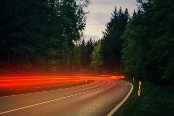 Dynamic light trails of cars on a forest highway captured with long exposure during twilight.
