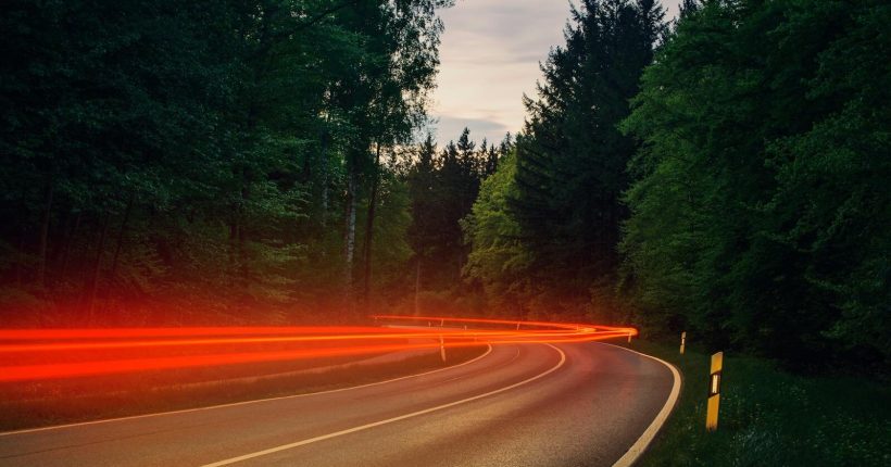 Dynamic light trails of cars on a forest highway captured with long exposure during twilight.