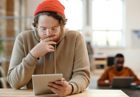 Man in a beanie and glasses using tablet in a bright, modern office.
