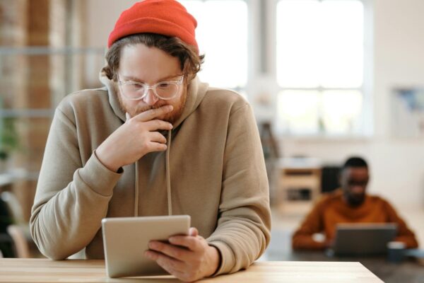 Man in a beanie and glasses using tablet in a bright, modern office.