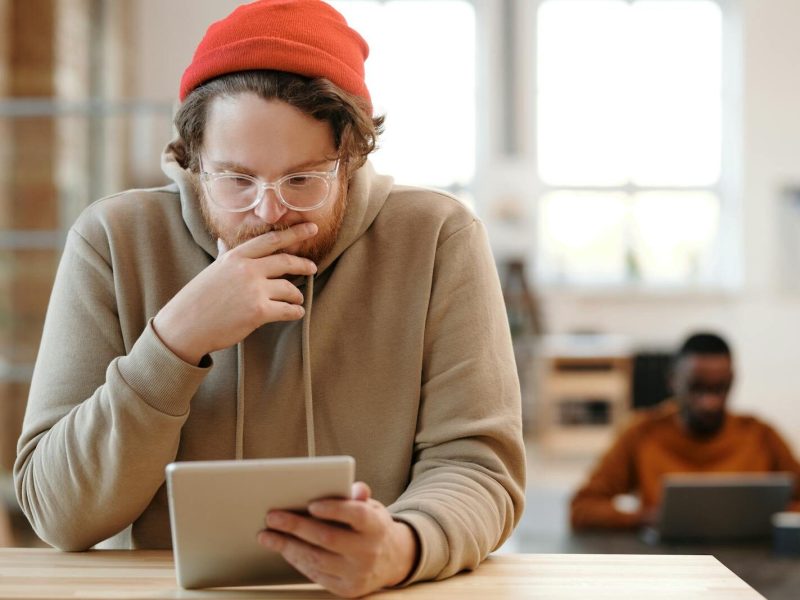 Man in a beanie and glasses using tablet in a bright, modern office.