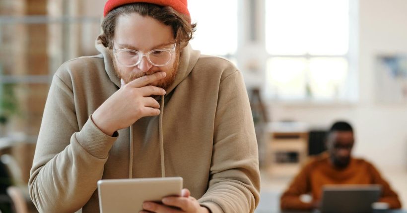 Man in a beanie and glasses using tablet in a bright, modern office.