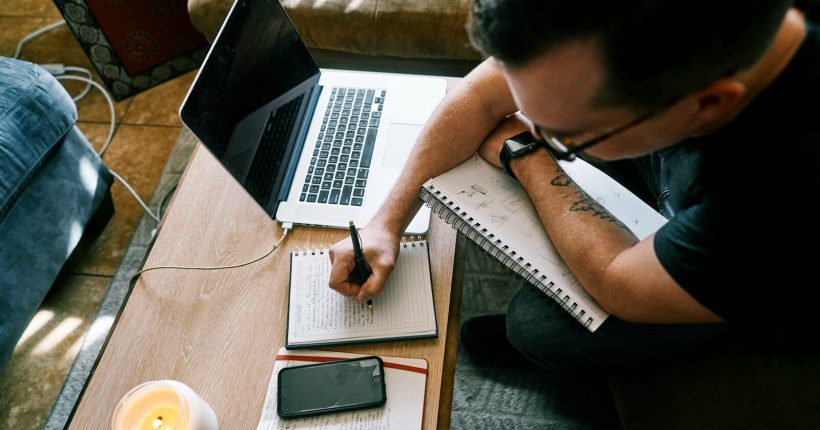 man in black t-shirt writing on white paper