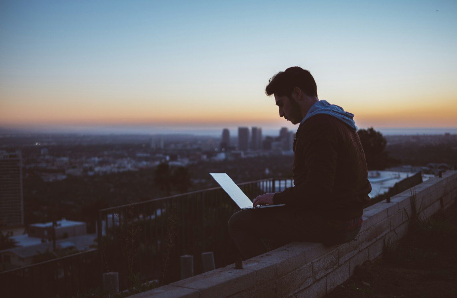 man sitting on concrete brick with opened laptop on his lap