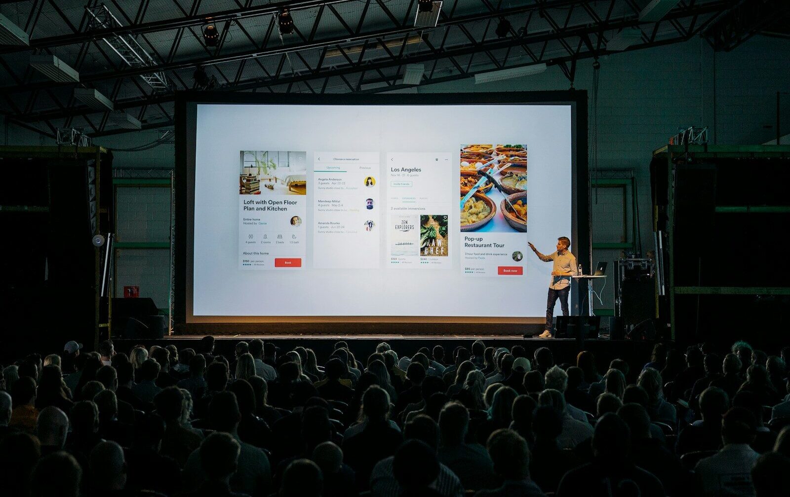 person discussing while standing in front of a large screen in front of people inside dim-lighted room