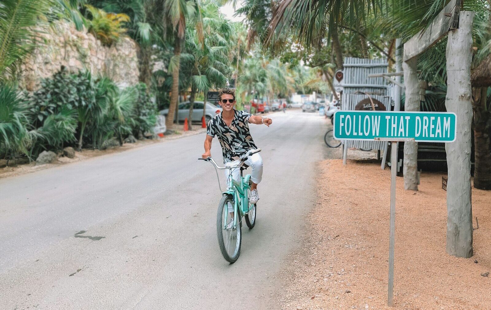 man rides bike pointing to follow that dream signage