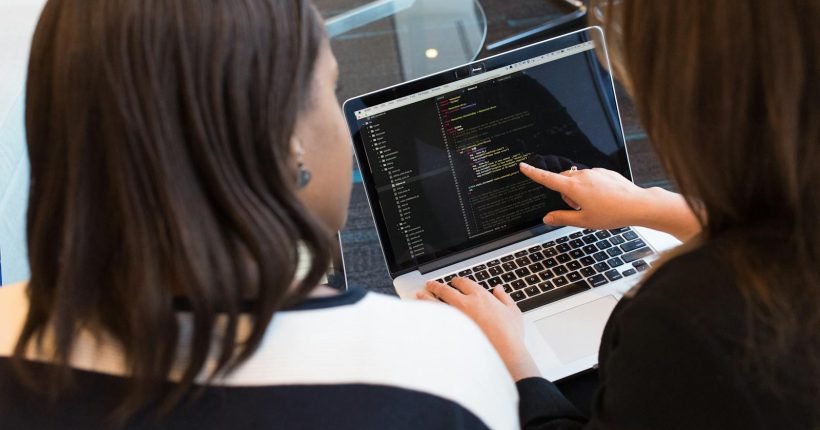 Two women working together on software programming indoors, focusing on code.