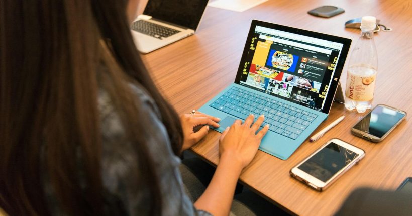 A woman working on a laptop at a wooden table with office devices around her.