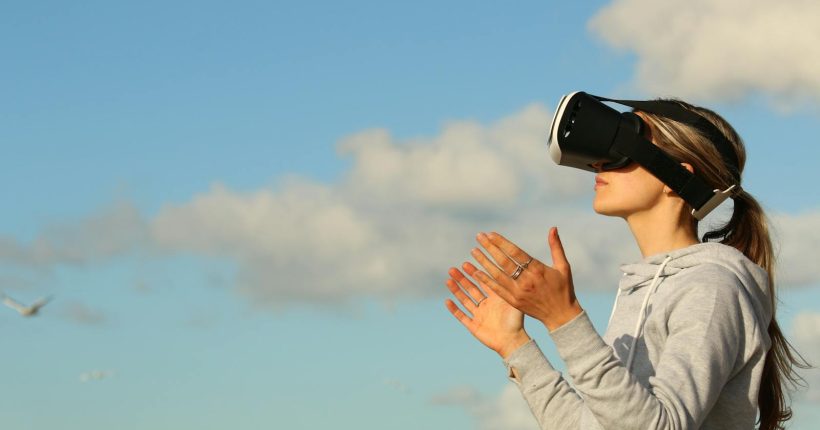 Woman using VR headset outdoors, exploring virtual reality under a clear blue sky.