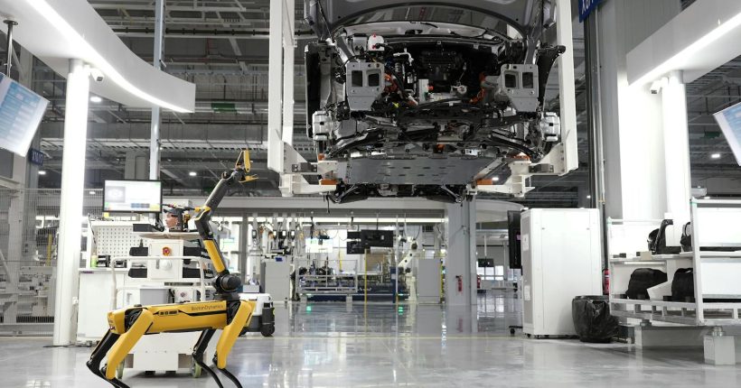 A robotic dog oversees an automated car assembly in a high-tech factory setting.