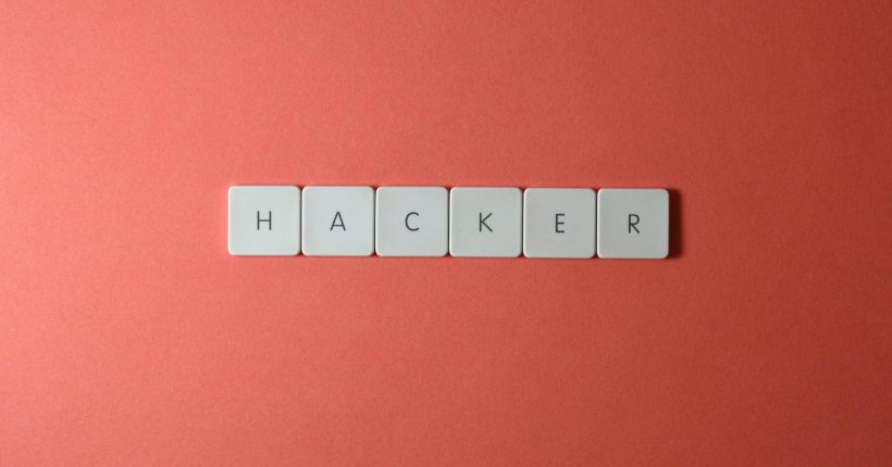 Close-up of the word 'HACKER' made with letter tiles on a red background, emphasizing cybersecurity.