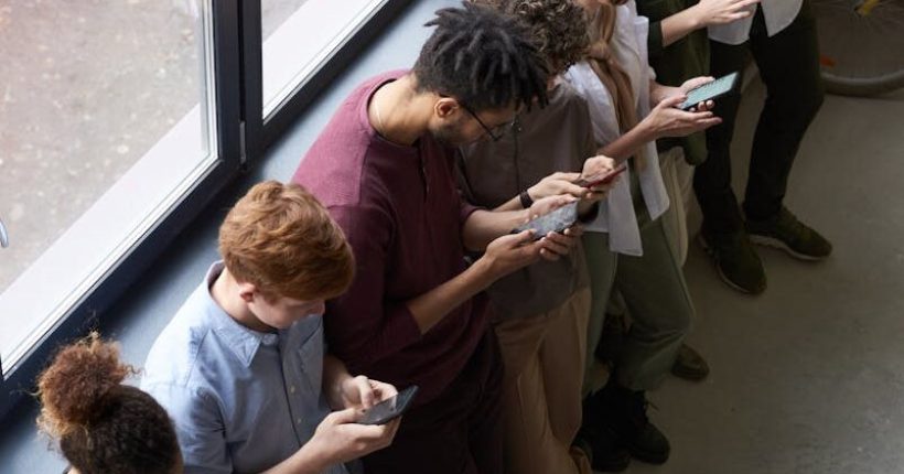 A group of diverse office workers standing by a window using smartphones, capturing modern workplace connectivity.