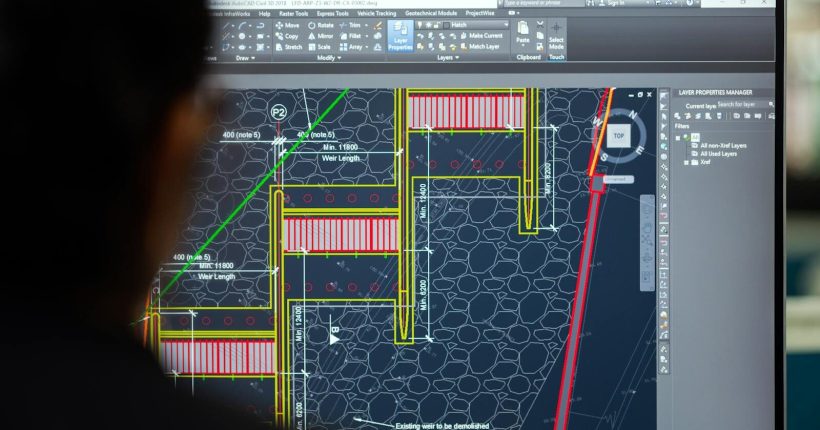 A civil engineer working on a weir design using CAD software on a computer screen in an office setting.