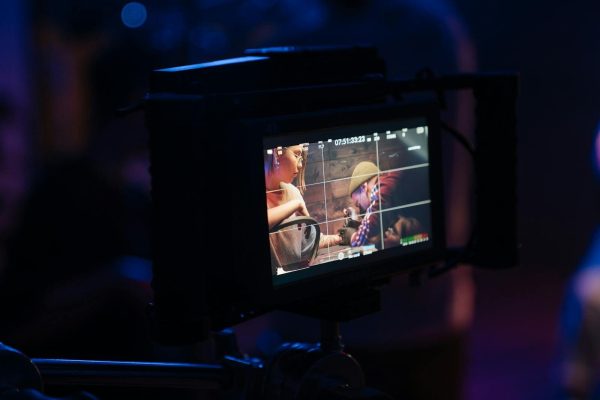 Film crew adjusting camera settings on set highlighted by neon lights.