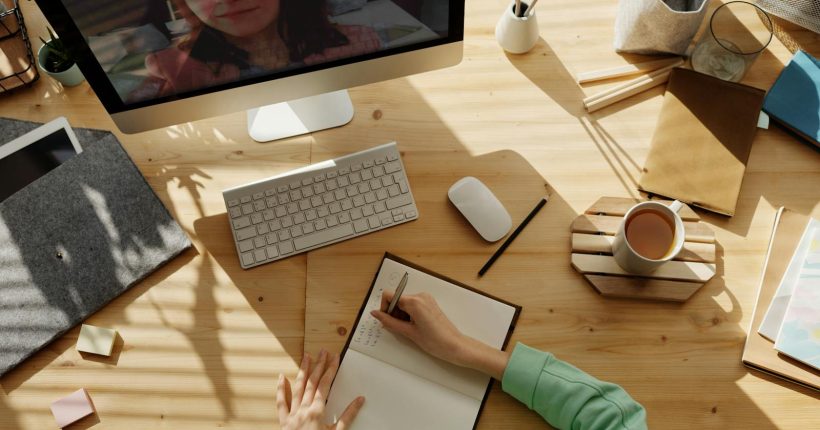 A student taking notes during a video call for online learning at home.