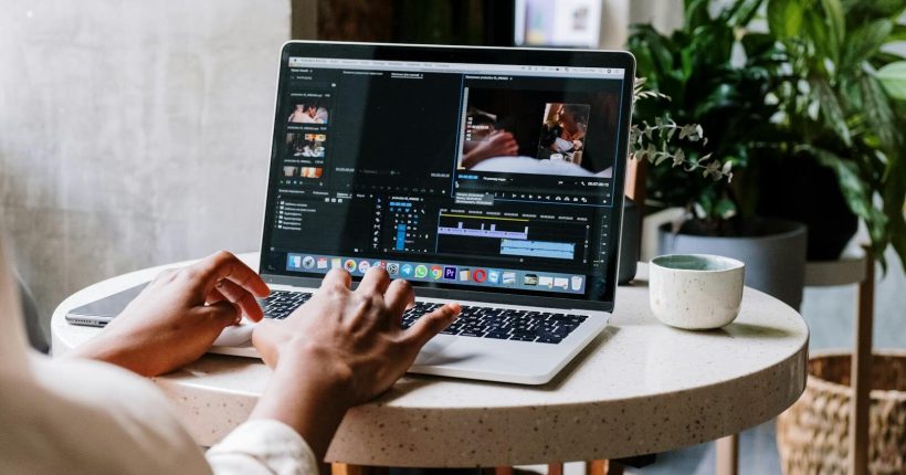 Freelance video editor working on a laptop in a cafe setting, utilizing Adobe software.