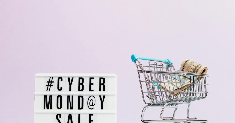 Shopping cart filled with cash beside a Cyber Monday sale sign, perfect for retail promotions.
