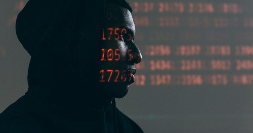 Side profile of a man in a hoodie, surrounded by red code, depicting cybersecurity theme.