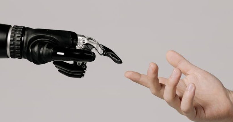 A human hand reaching to touch a bionic prosthetic hand on a white background.