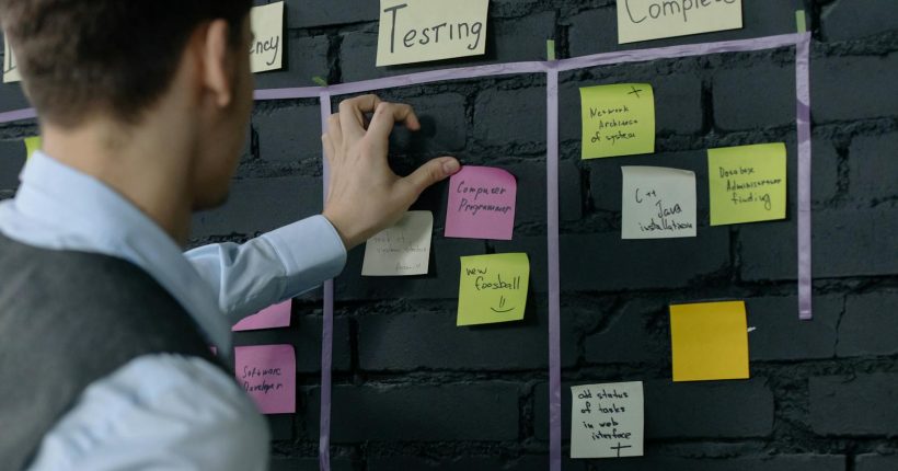 Man organizing project tasks on a wall using sticky notes in a modern office setting.