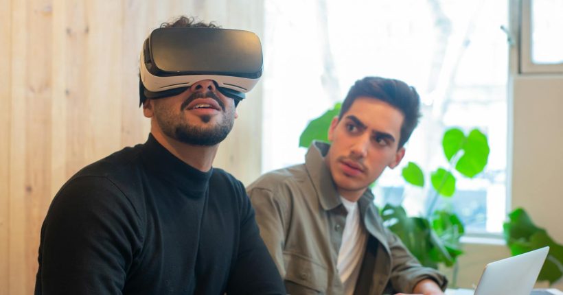 Two adult men engaged with virtual reality and laptop technology in a contemporary office.
