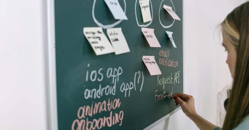 Woman writing on chalkboard during a brainstorming session in an office setting.