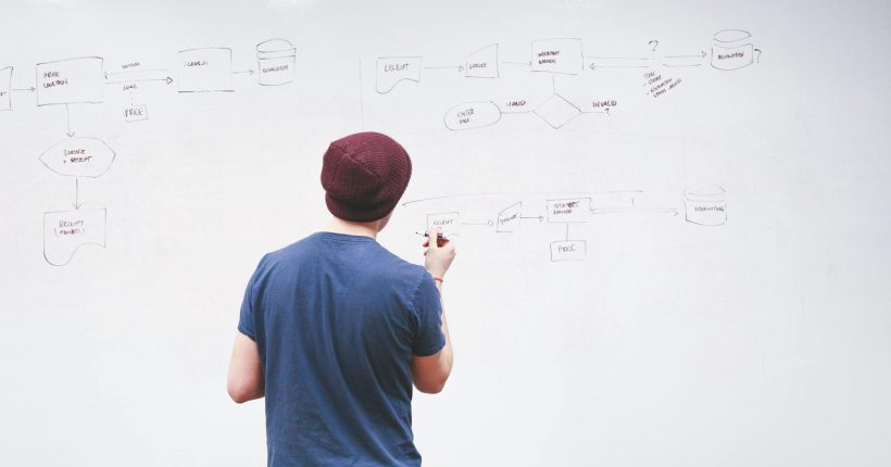 Young man brainstorming and planning a project on a whiteboard with diagrams and notes.