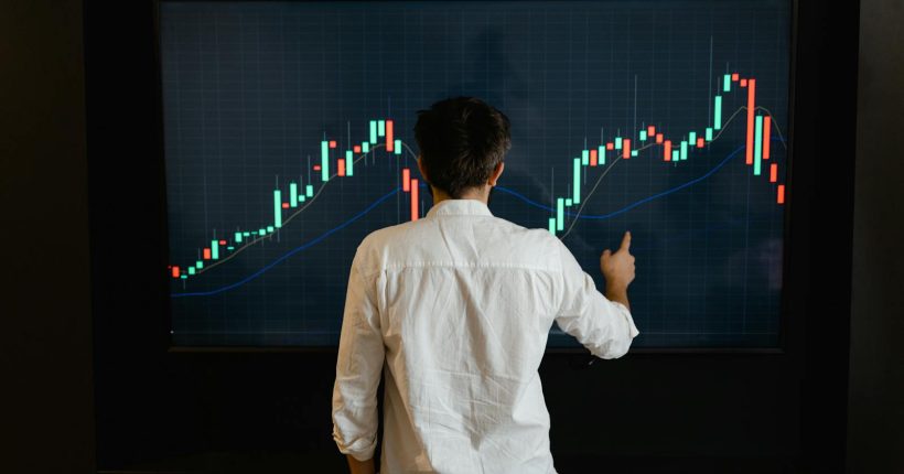Adult male reviewing stock market data on a large display screen indoors.