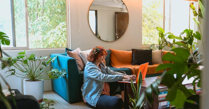 Woman working remotely from a cozy living room surrounded by plants.