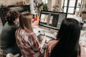 A group of young adults working on a design project using a desktop computer in an artistic workspace.