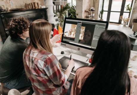 A group of young adults working on a design project using a desktop computer in an artistic workspace.