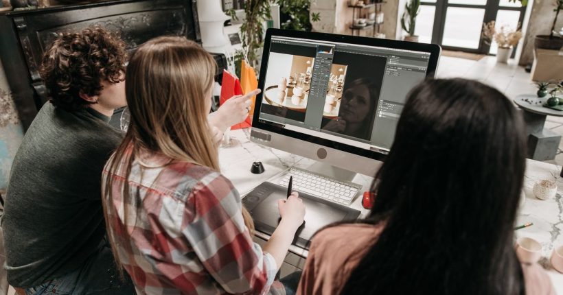 A group of young adults working on a design project using a desktop computer in an artistic workspace.