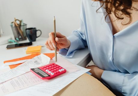 A woman is calculating expenses using a calculator and papers at her desk.