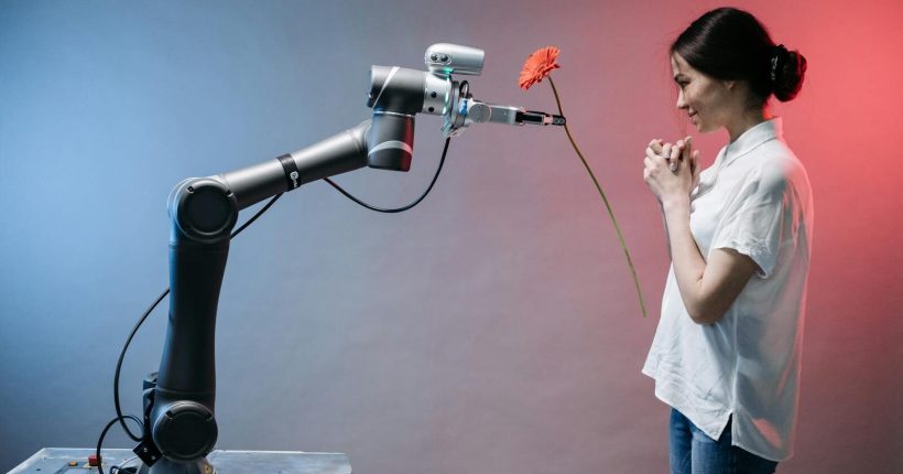 A robotic arm offers a flower to a woman in a display of technology and human connection.