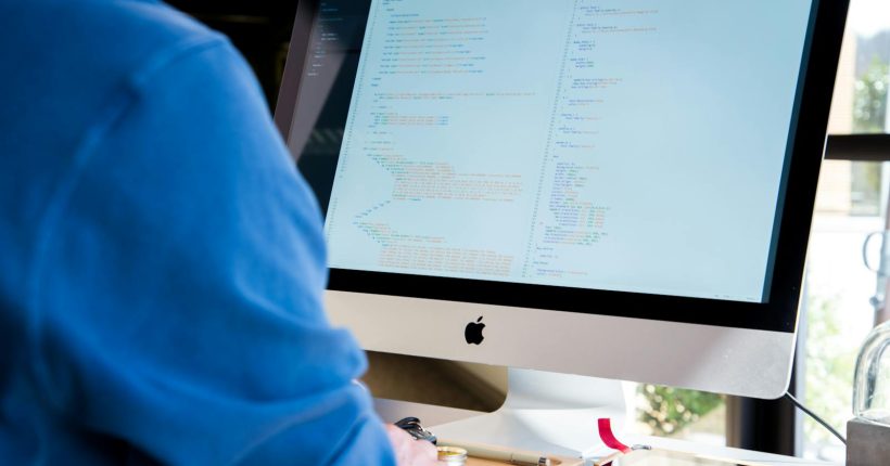 A programmer in a blue shirt coding on an iMac. Perfect for technology or work-related themes.