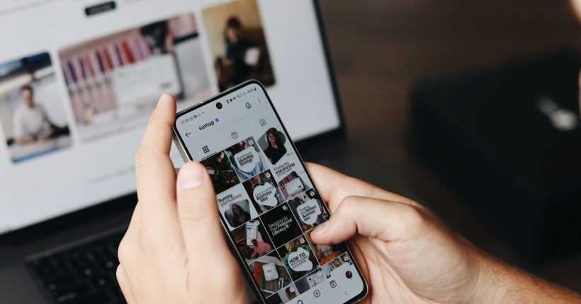 A person holding a cell phone in front of a laptop