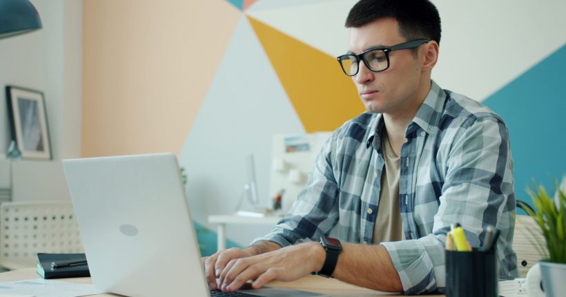 Man wearing glasses types on a laptop at a desk.