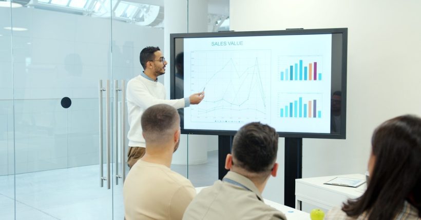 Man presenting charts on a large screen to audience.