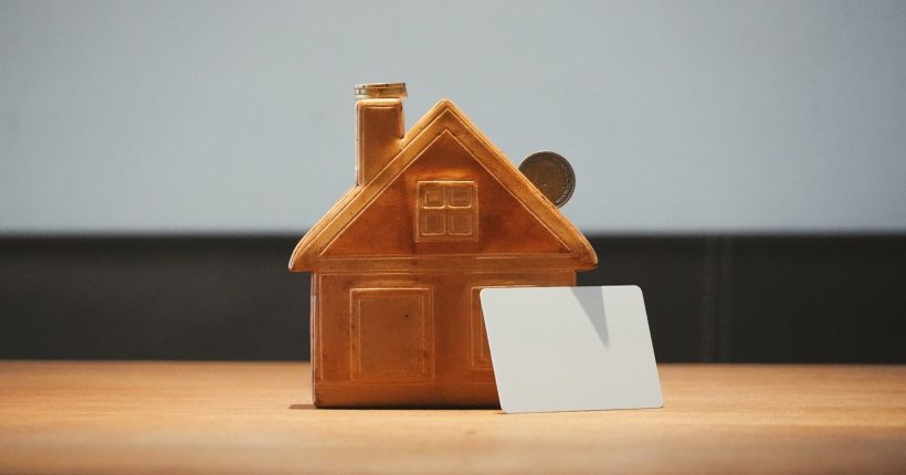 A small house bank with a coin and blank card.