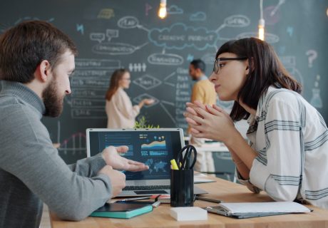 Two colleagues discussing charts on a laptop screen.