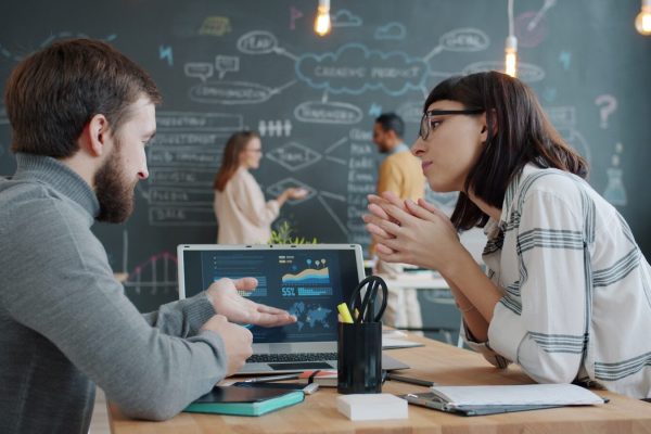 Two colleagues discussing charts on a laptop screen.