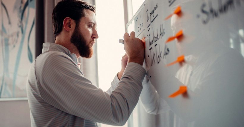 a man writing on a white board with orange markers