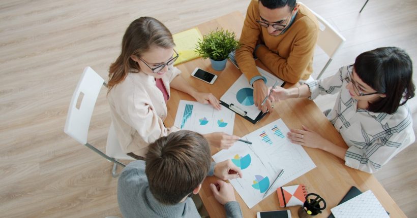 Four people collaborating around a table with charts.