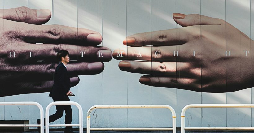 man walking on sidewalk beside hands mural