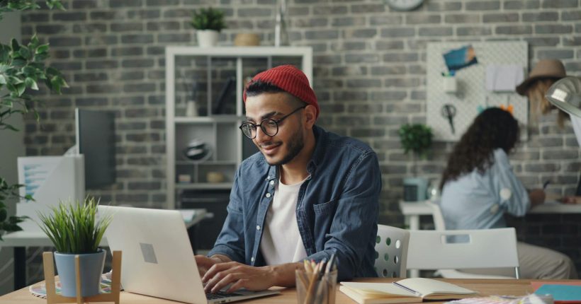 a man in a red hat is working on his laptop