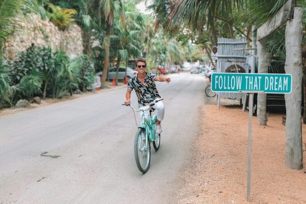 man rides bike pointing to follow that dream signage