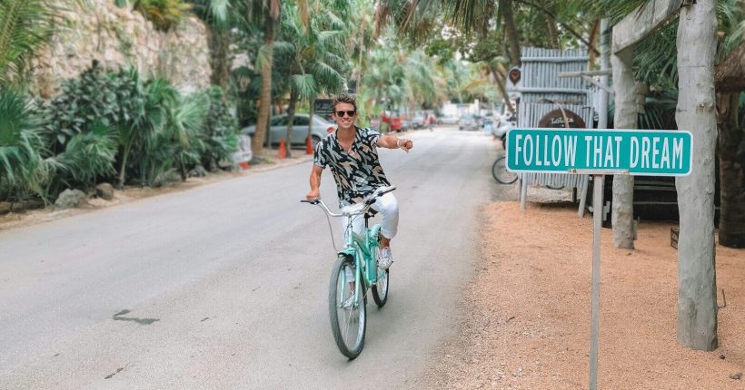 man rides bike pointing to follow that dream signage