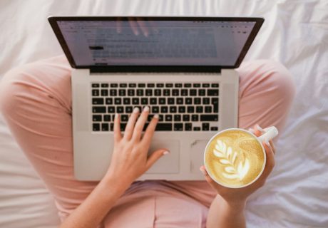 person using MacBook Pro and holding cappuccino